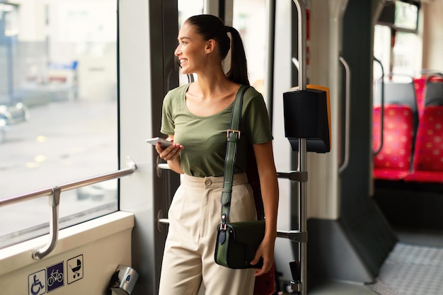 Frau benutzt Mobiltelefon und steht in der städtischen Straßenbahn beim Pendeln