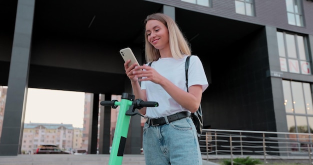 Frau benutzt Smartphone nach Fahrt mit elektrischem Tretroller Ökologischer Transport