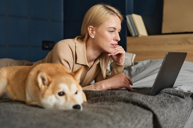 Frau benutzt zu Hause einen Laptop, ihr Hund liegt in der Nähe