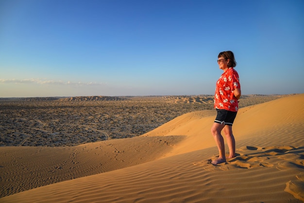 Frau beobachtet den Sonnenuntergang über den Sanddünen der arabischen Wüste in Oman