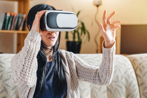 Frau berührt etwas mit Virtual-Reality-Headset-Brille und sitzt zu Hause auf der Couch