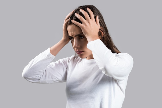 Frau berührt ihre Schläfen und fühlt Stress auf grauem Hintergrund. Frau leidet unter Kopfschmerzen. Verzweifelt gestresst, weil Schmerzen und Migräne. Frau mit starken Kopfschmerzen, die Hände auf dem Kopf hält