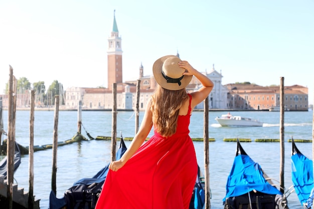 Frau besucht Venedig in Italien. Hintere Ansicht der schönen jungen Frau im roten Kleid, die Ansicht der venezianischen Lagune genießt.