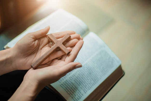 Frau betet mit Bibel und Holzkreuz.