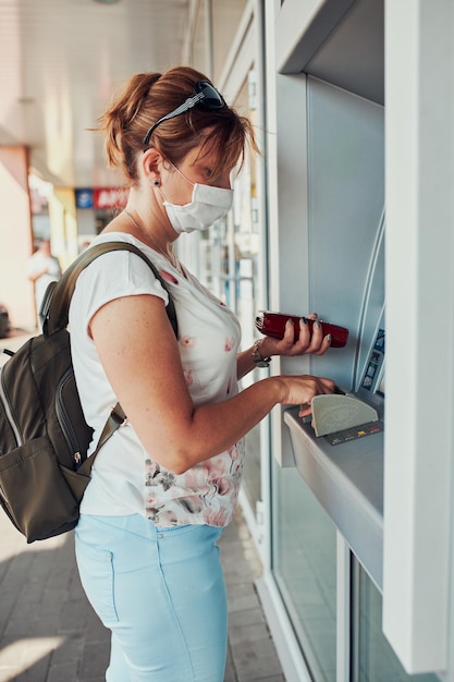 Foto frau bezieht geld aus dem geldautomaten mit einer debit- oder kreditkarte, die draußen auf der straße steht