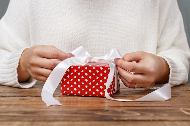 Frau bindet einen Bandbogen auf ein eingewickeltes Geschenk Nahaufnahme