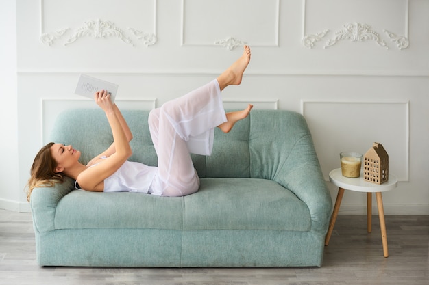 Frau bleiben zu Hause und haben eine gute Zeit mit interessanten Buch auf modernen Sofa zu Hause