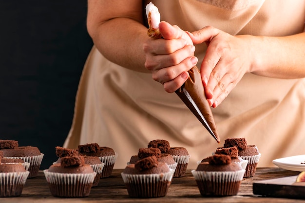 Frau dekoriert Muffins mit Schokoladencreme in der Küche Pastrycook Hand bereiten Schokoladen-Cupcakes zu