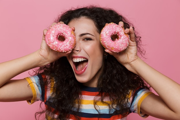 Frau der 20er Jahre mit lockigem Haar, die Spaß hat und Donuts isoliert auf Rosa hält