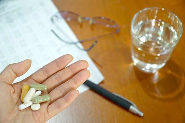 Frau der linken Hand, die Droge und Vitamin auf Arbeitsplatzhintergrund hält. Wasserglas.