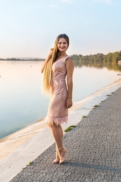 Frau, die Abendpfirsichfarbenkleid gegen See trägt