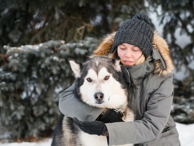 Frau, die alaskisches Malamute im Winterwald umarmt