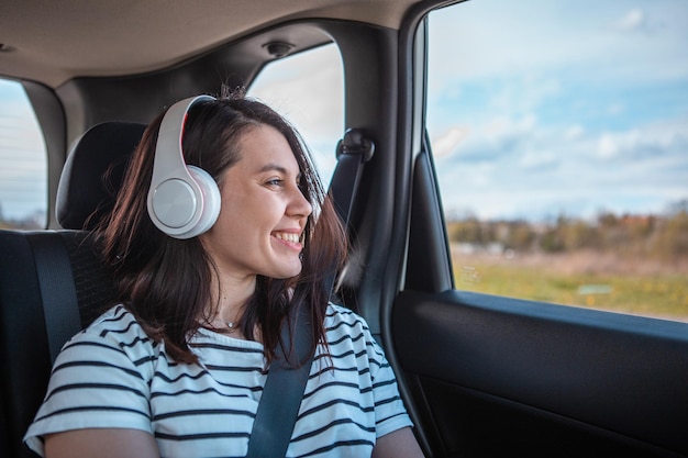 Frau, die am Autoheck sitzt, sitzt und hört Musik mit Kopfhörerkopierraum, sonniger Tag