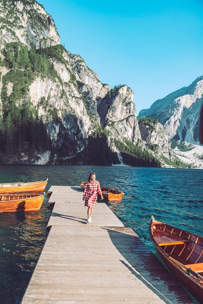 Foto frau, die am bergseepier mit holzbooten im roten kleid spazieren geht