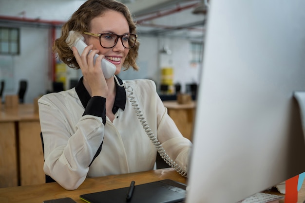 Frau, die am Festnetztelefon am Schreibtisch spricht