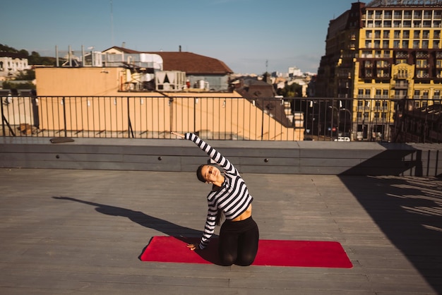 Frau, die am frühen Morgen Yoga-Übungen auf dem Hausdach macht