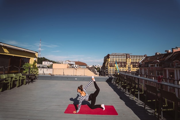 Frau, die am frühen Morgen Yoga-Übungen auf dem Hausdach macht