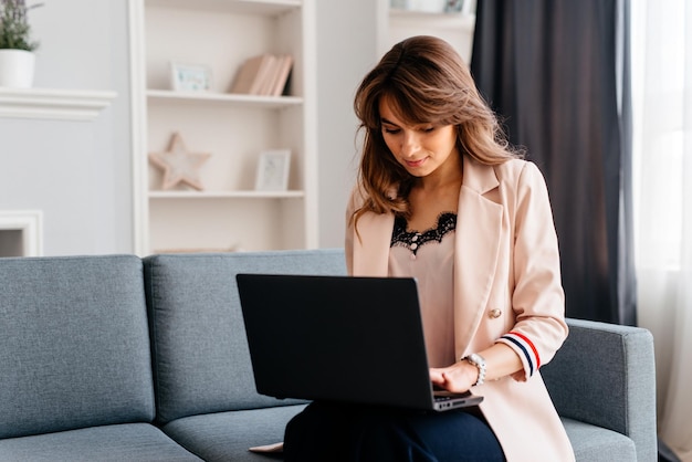 Frau, die am Laptop arbeitet, sitzt aufgrund der Quarantäne auf dem Sofa und arbeitet zu Hause