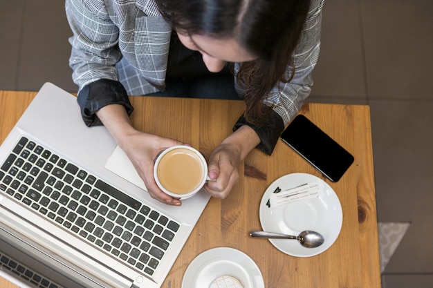 Foto frau, die am laptop arbeitet und frischen kaffee trinkt