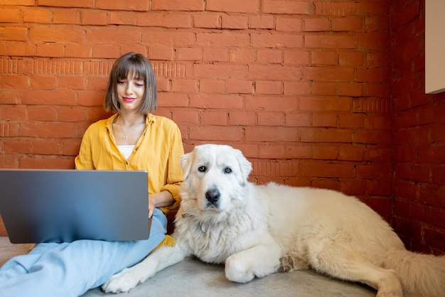 Frau, die am Laptop arbeitet, während sie zu Hause mit ihrem Hund sitzt