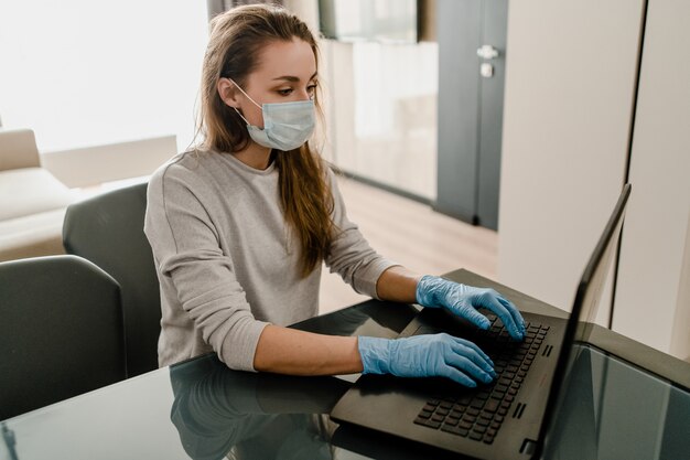 Frau, die am Laptop vom Hauptbüro arbeitet, das Maske und Handschuhe trägt