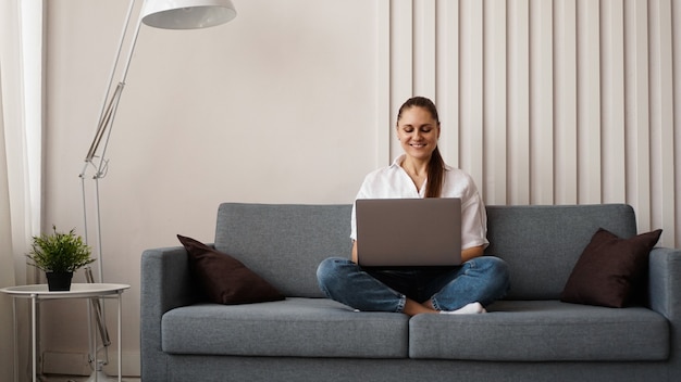 Frau, die am Laptop von zu Hause oder vom Studenten arbeitet, der von zu Hause oder vom Freiberufler studiert. Moderne Geschäftsfrau in einem weißen Hemd und in Jeans.