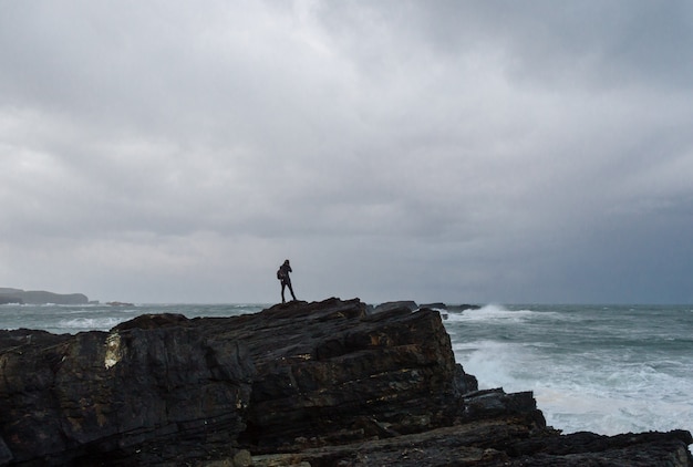 Frau, die am Rand einer Klippe vor einem Sturm im kantabrischen Meer fotografiert.