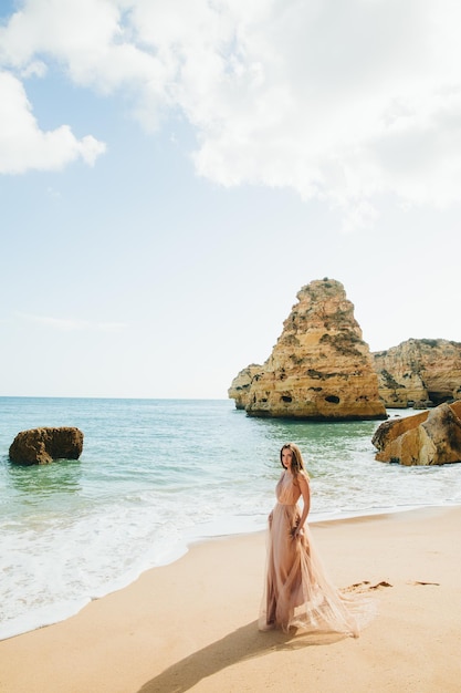 Frau, die am Strand entlang gegen die Felsen und das Meer geht