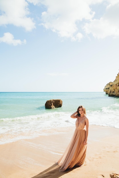 Frau, die am Strand entlang gegen die Felsen und das Meer geht