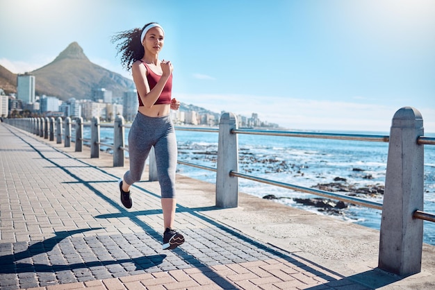 Frau, die an der Meerespromenade für Fitnessenergie und starken Körper in Kapstadt läuft Läuferin, Sportlerin und Athletin am Meer für Marathon-Cardio-Übungen und gesundes Sommertraining in der Sonne