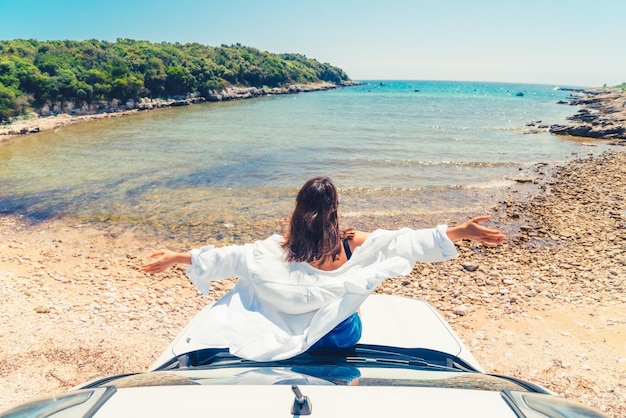 Frau, die an der Motorhaube mit Blick auf den Sommerstrand liegt