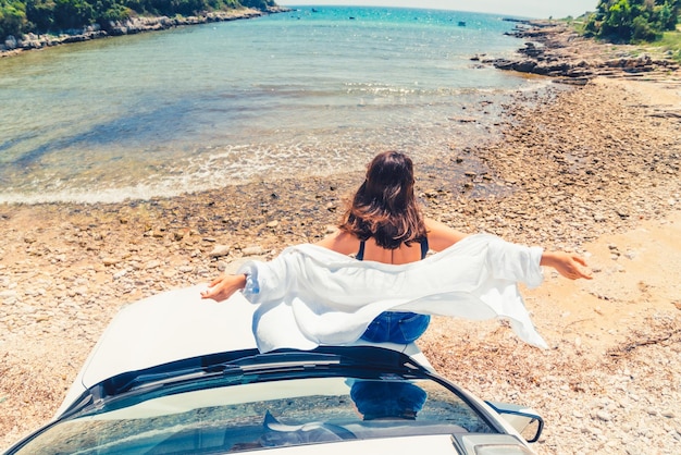 Frau, die an der Motorhaube mit Blick auf den Sommerstrand liegt