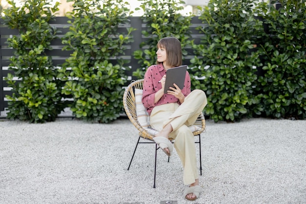 Frau, die an einem digitalen Tablet arbeitet, während sie entspannt im Hinterhof sitzt