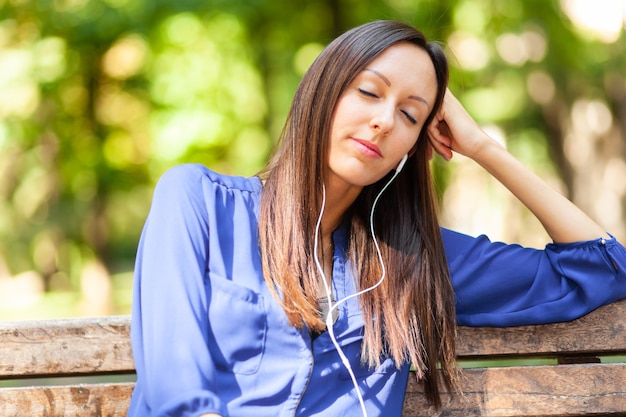 Frau, die an einem heißen sonnigen Sommertag auf einer Bank in einem Park Musik hört