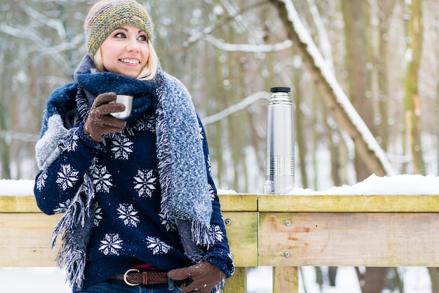 Frau, die an einem kalten Wintertag einfriert, der sich mit heißem aufwärmt