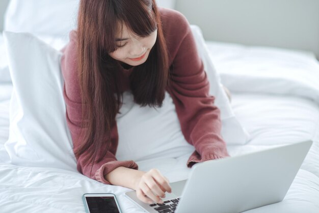 Frau, die an einem Laptop arbeitet, der auf dem Bett im Haus sitzt