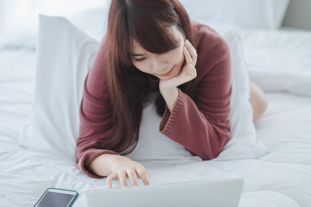 Frau, die an einem Laptop arbeitet, der auf dem Bett im Haus sitzt