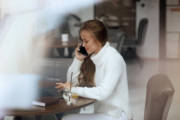 Frau, die an einem Laptop arbeitet und mit dem Handy spricht