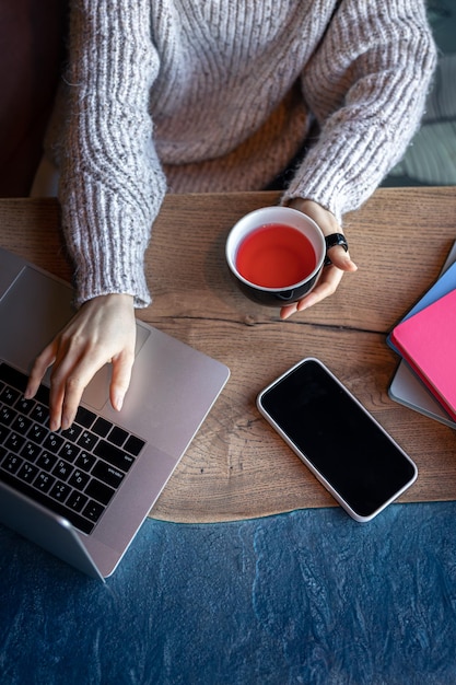 Frau, die an einem Laptop in einem Café mit Draufsicht einer Tasse Tee arbeitet