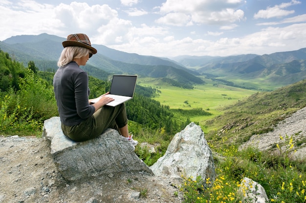 Frau, die an ihrem Computer oben auf dem Berg arbeitet.