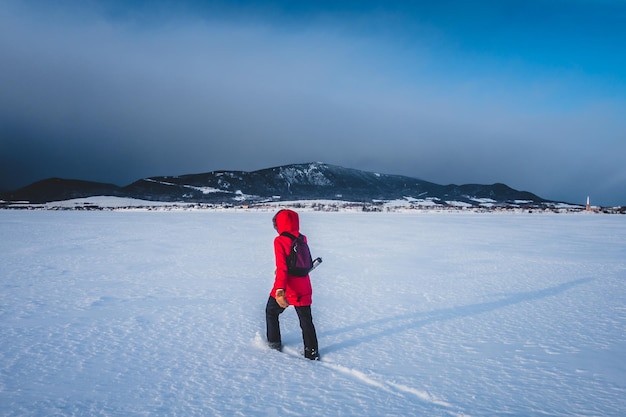 Foto frau, die an kalten wintertagen einsam auf einem zugefrorenen see spazieren geht