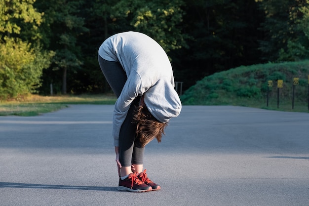 Frau, die Anfänger-Yoga-Übung für das Strecken im Park tut. Weibliche Person, die sich vor dem Joggen im Freien streckt