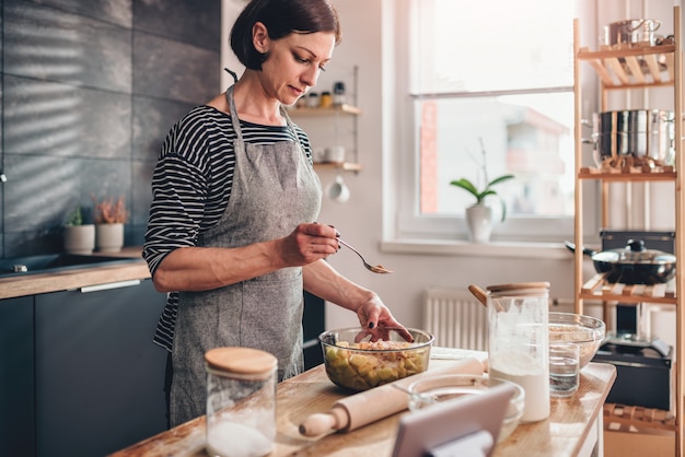 Frau, die Apfelkuchen auf Holztisch macht