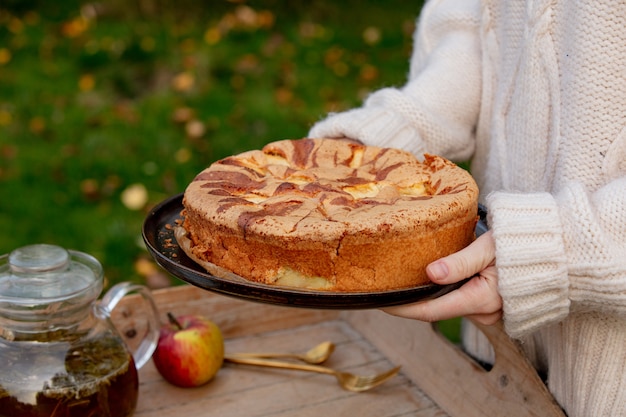 Frau, die Apfelkuchen und Tee auf Behälter auf Tabelle in einem Garten hält