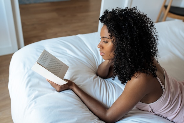 Frau, die auf Bett liegt und ein Buch liest