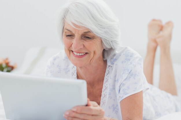 Frau, die auf Bett liegt und eine Tablette verwendet