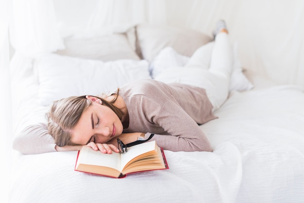 Frau, die auf Bett mit Brillen über dem offenen Buch schläft