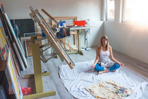 Frau, die auf dem Boden sitzt und Yoga in ihrem Kunststudio durchführt.