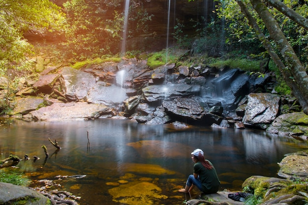 Frau, die auf dem Felsen betrachtet den Wasserfall sitzt