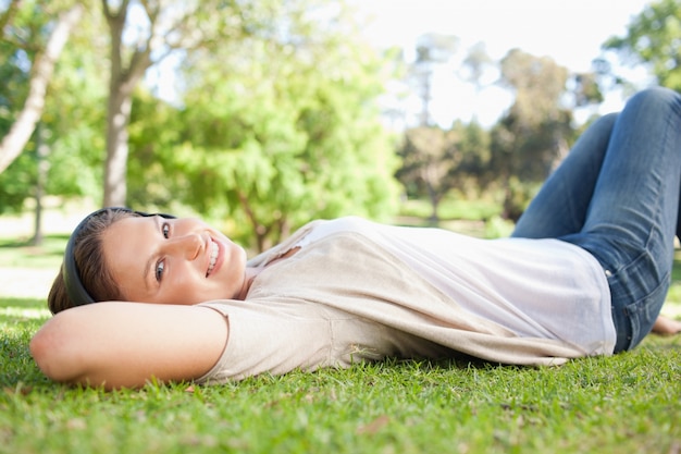 Frau, die auf dem Gras beim Hören Musik liegt